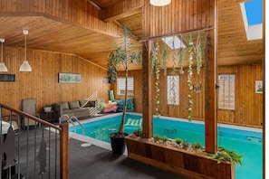 Un intérieur en bois avec une piscine, un canapé et des plantes suspendues.
