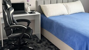 Een slaapkamer met een bed, een bureau met een stoel, een laptop en een vaas met bloemen.