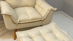 Een beige fauteuil met houten poten en een bijpassend pouf.