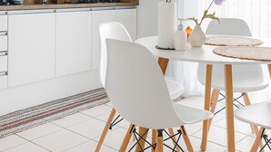 Een moderne keuken met witte kasten, een eetgedeelte met witte stoelen en een houten tafel, en een raam met uitzicht op gebouwen.