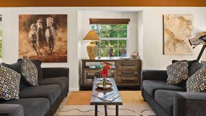 Ein Wohnzimmer mit zwei Sofas, einem Couchtisch, einer Lampe, einer Vase mit Blumen und Kunstwerken an den Wänden.