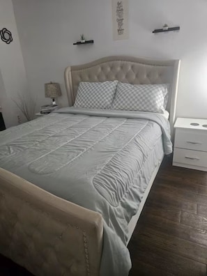 Een slaapkamer met een bed, nachtkastje, lamp en een decoratie aan de muur.
