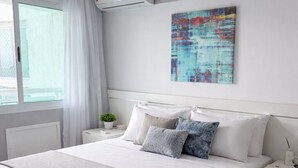 A modern bedroom with a large bed, a bedside table, an air conditioning unit, and a window with curtains. - LUXURY penthouse 6 people seafront pedra do pontal (Rio de Janeiro)