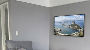A grey sofa in a room with a tiled floor and a framed picture of a coastal landscape on the wall. - LUXURY penthouse 6 people seafront pedra do pontal (Rio de Janeiro)