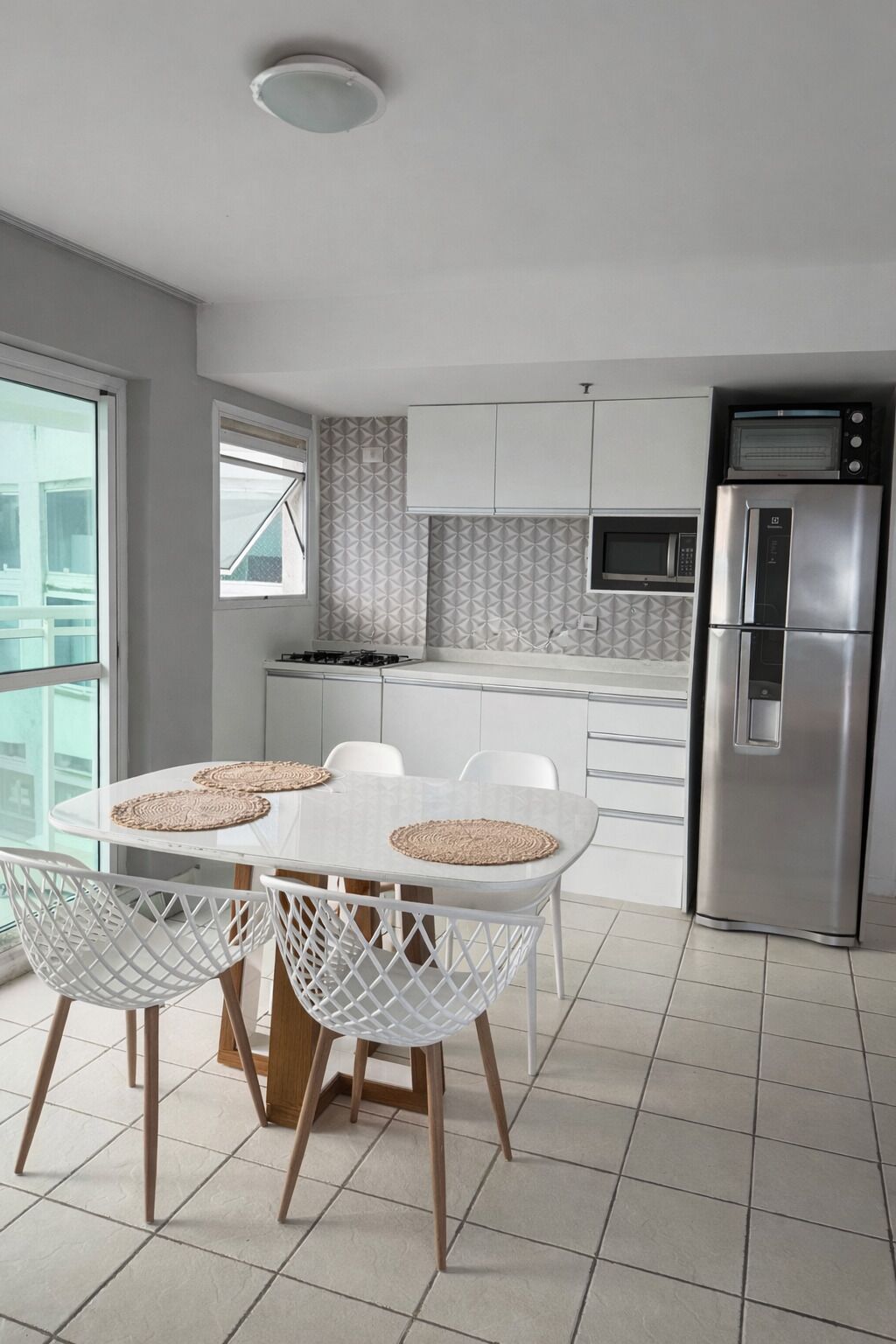 Una cocina moderna con armarios blancos, microondas integrado y refrigerador de acero inoxidable.