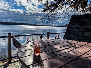 A table with a glass of beer, a view of a lake, and a stone wall.