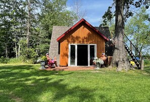 A small wooden cabin with a red roof, a sliding glass door, and a brick patio.