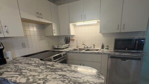 A modern kitchen with white cabinets, a marble countertop, a dishwasher, and a microwave.