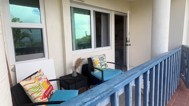 A balcony with a blue railing, two chairs with cushions, and a small table with a vase.