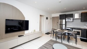 A modern kitchen with a built-in microwave, a refrigerator, and a dining area with a table and chairs. - Cozy One bed at Loxwood (Accra)