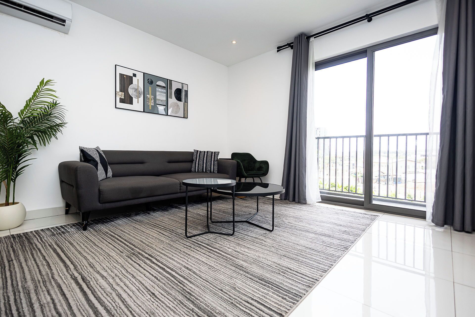 A modern living room with a sofa, a coffee table, a potted plant, and a large window with a view.