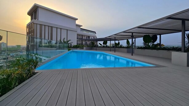 A rooftop swimming pool with a wooden deck, surrounded by modern buildings and a clear sky. - Cozy One bed at Loxwood (Accra)