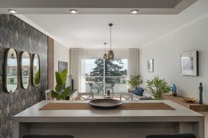 A modern living room with a dining area, large windows, and a view of the city. - Madeira Ocean Paradise – Balcony with Sea View (Caniço)