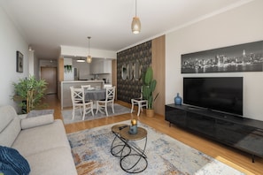 A modern living room with a sofa, a coffee table, a TV, and a dining area with chairs and a table. - Madeira Ocean Paradise – Balcony with Sea View (Caniço)
