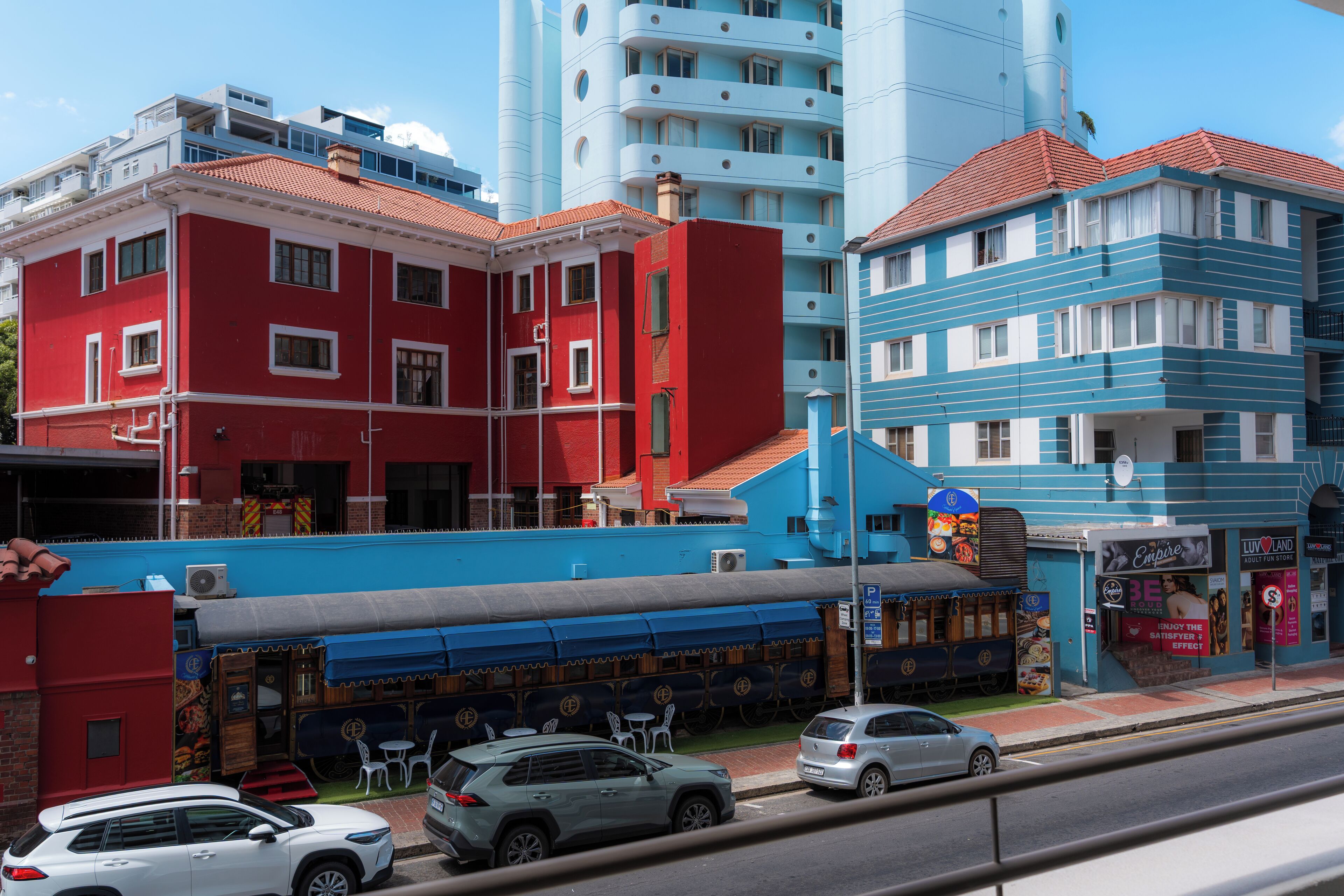 A street view with a red building, a blue building, and a restaurant with outdoor seating.