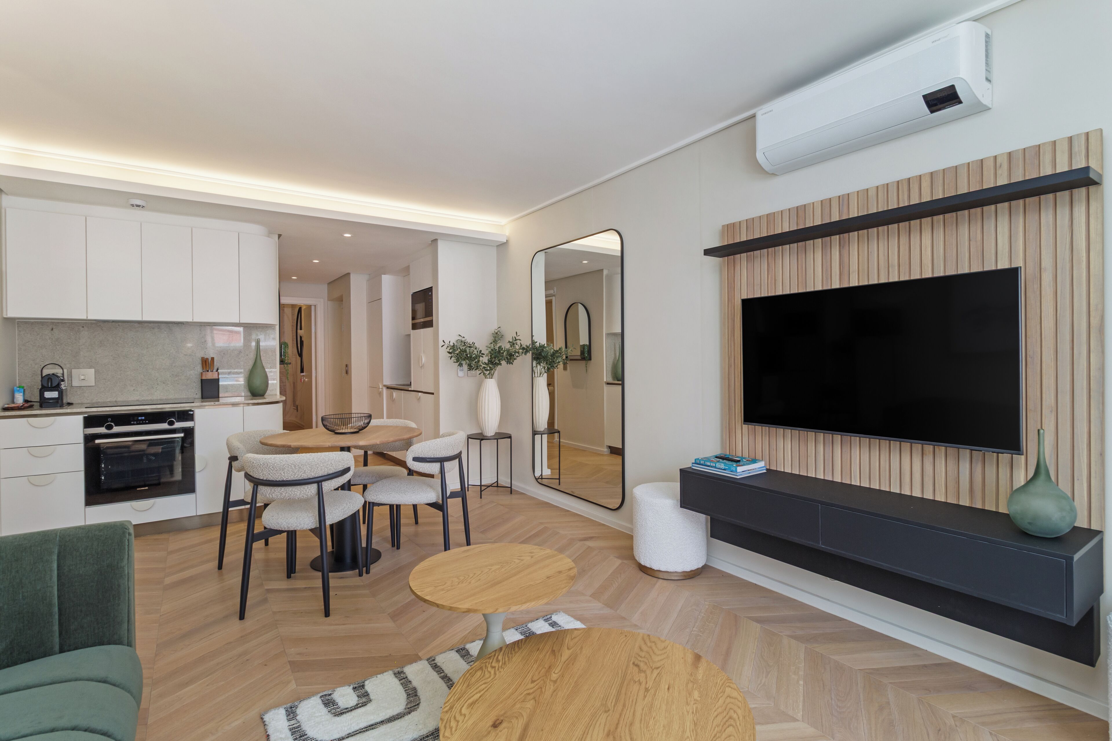 Een moderne woonkamer met een televisie, zitplaatsen en een keukenhoek.