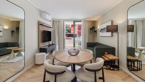Ein modernes Wohnzimmer mit einem runden Holztisch, zwei Sesseln, einem grünen Sofa und einem Fernseher.