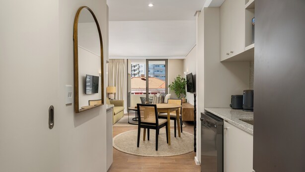 A compact kitchen with a dishwasher, a dining area with a round table and chairs, and a large mirror on the wall. - Dolce Vita | Lush Sea Point Gem with Balcony (Cape Town)