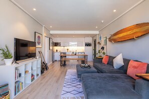 Una sala de estar moderna con un sofá gris, un televisor de pantalla plana y una tabla de surf de madera en la pared.