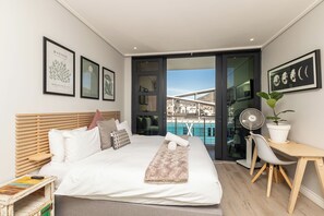 Un dormitorio moderno con cama, mesita de noche y vistas a una piscina y un edificio.