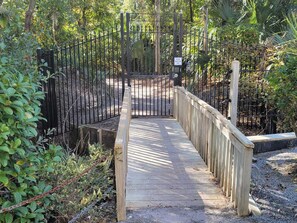 A wooden boardwalk leading to a gated entrance surrounded by dense foliage. - Brigantine Quarters 2-bedroom condo in Shipyard--discounted August weeks! (Hilton Head Island)