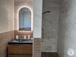 Une salle de bain avec un mur en marbre, un meuble-lavabo en bois et un espace douche.