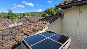 Un toit-terrasse équipé de panneaux solaires, un toit recouvert de tuiles et une vue sur une zone boisée.