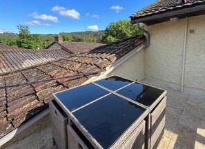 Ein Dach mit Solaranlage, Ziegeldach und Blick auf ein bewaldetes Gebiet.