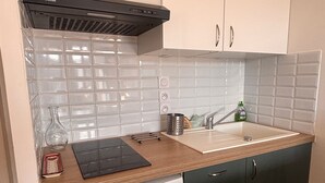 Eine kompakte Küche mit weiß gefliestem Fliesenspiegel, einer Holz Arbeitsplatte, einem eingebauten Geschirrspüler und einer schwarzen Dunstabzugshaube.