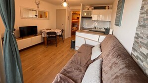 Ein gemütlicher Wohnraum mit Küchenzeile, Essbereich und einer Sitzecke mit Sofa und Fernseher.