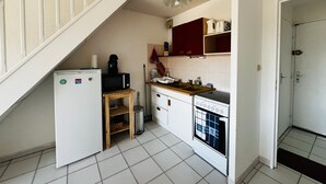 Kompakti keittiö, jossa on jääkaappi, mikroaaltouuni, liesi ja puinen pöytä.