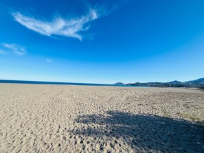 En bred, öppen sandstrand med en klarblå himmel och avlägsna berg.