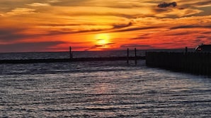 A sunset over the ocean with a wooden pier extending into the water. -  Campfire Bliss at the Beach 
Eastern Shore Virginia Cottage Getaway (Horntown)