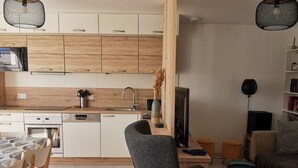 Moderni keittiö, jossa on puiset kaapit, ruokailutila pöytineen ja tuoleineen, televisio ja kirjahylly.