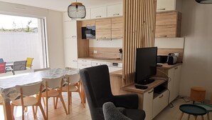 Moderni keittiö, jossa on puiset kaapit, mikroaaltouuni ja televisio. Keittiössä on myös ruokailutila, jossa on pöytä ja tuolit.