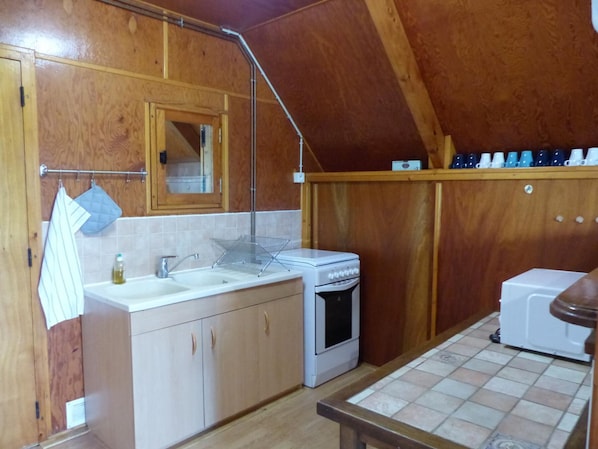 Une cuisine de taille réduite, dotée de meubles de rangement en bois, d’un évier, d’une cuisinière et d’un petit plan de travail.