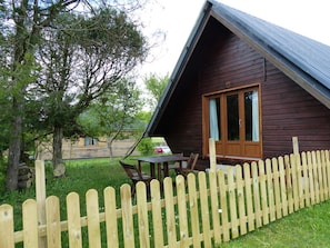 Une cabane en bois avec un toit en pente, une porte en bois et une petite véranda comprenant une table et des chaises.