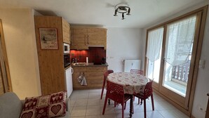 A compact living space with a kitchenette, a dining area with a table and chairs, and a sofa with patterned cushions. - Studio cabin in the center - 4 guests (Les Carroz d'Arâches)