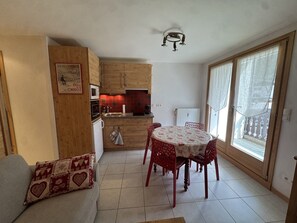 A compact living space with a kitchenette, a dining area with a table and chairs, and a sofa with patterned cushions. - Studio cabin in the center - 4 guests (Les Carroz d'Arâches)