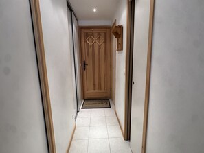 A hallway with a wooden door, white walls, and a tiled floor. - Studio cabin in the center - 4 guests (Les Carroz d'Arâches)