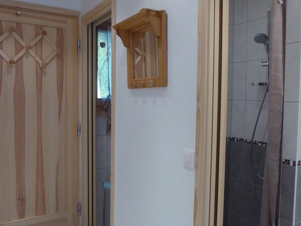 A wooden door with a diamond pattern, a small wooden shelf, and a shower area with tiled walls. - Studio cabin in the center - 4 guests (Les Carroz d'Arâches)