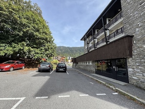 Eine Straße mit geparkten Autos, ein Gebäude mit einer Stein-Fassade und ein Berg im Hintergrund.