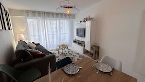 Una sala de estar moderna con un sofá, una mesa de comedor para cuatro personas, un televisor en la pared y una alfombra estampada.