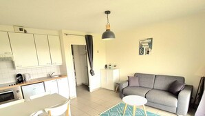 Ein kompakter Wohnbereich mit Küchenzeile, einem Essbereich mit Tisch und Stühlen, einem grauen Sofa, einem gemusterten Teppich und einer Pendelleuchte.