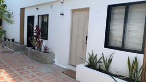 A modern building with a white exterior, a wooden door, and a window with blinds. There are potted plants and a metal chair outside. - Aerobeach Apartments (Cartagena de Indias)