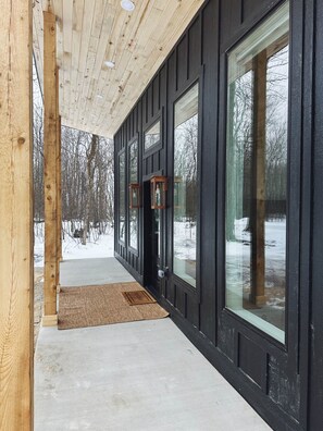 Un porche de madera con ventanas grandes y una puerta, que da a un paisaje nevado.
