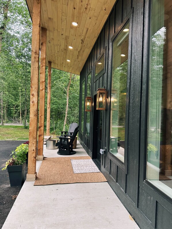 Un espacio al aire libre cubierto con techo de madera, ventanas de marco negro y una disposición de asientos con sillas y una mesa.