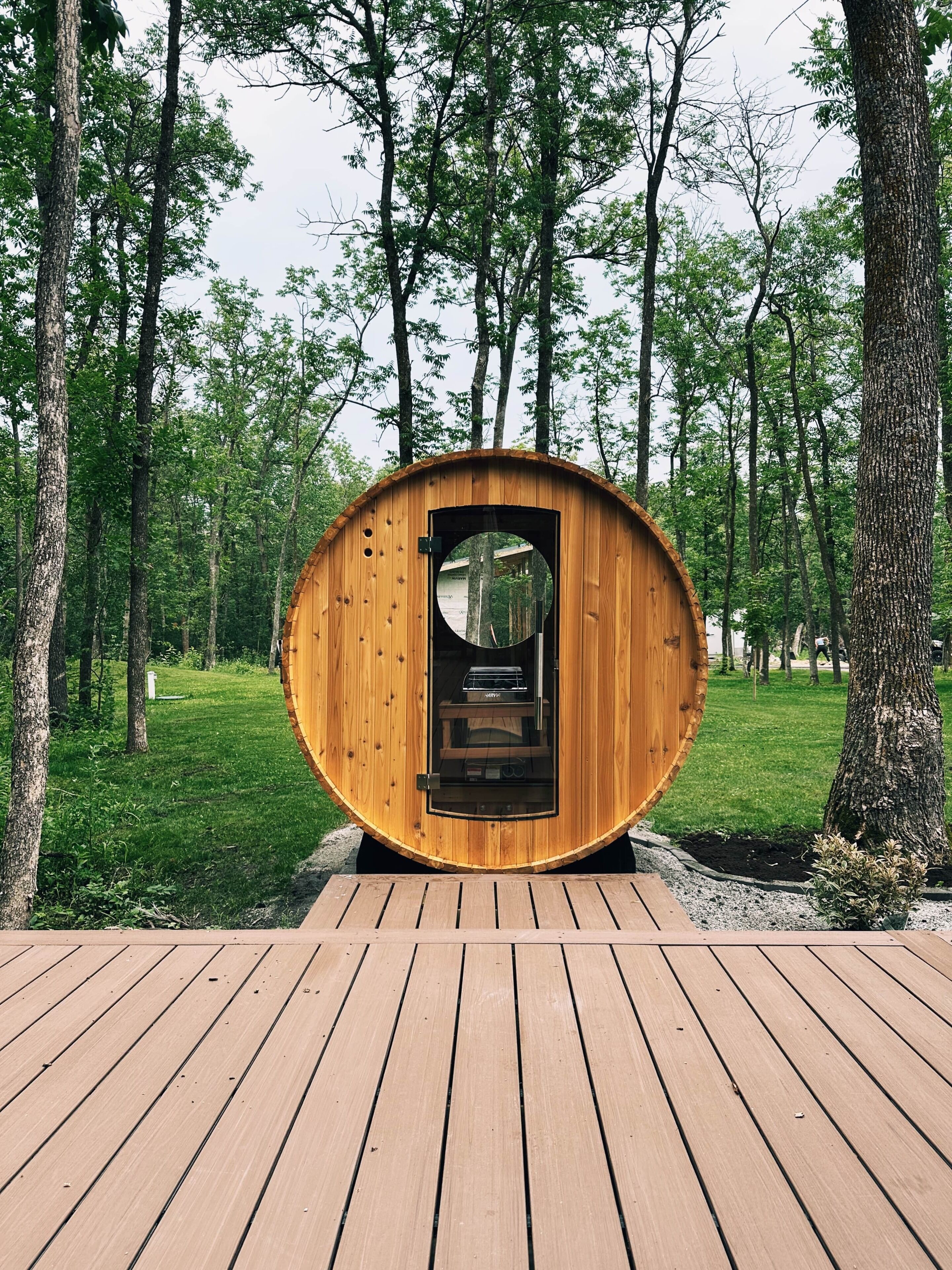 A wooden structure with a circular door, surrounded by a wooden deck, set in a forested area.