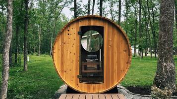 A wooden structure with a circular door, surrounded by a wooden deck, set in a forested area.