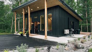 A modern cabin with a covered porch, large windows, and a gravel driveway.